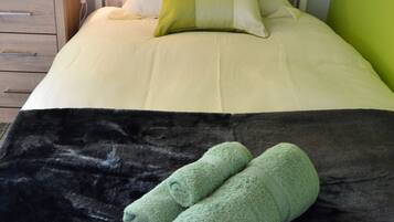 Een netjes opgemaakt bed met een zwart-wit dekbed, twee groene handdoeken en een lamp op een nachtkastje.