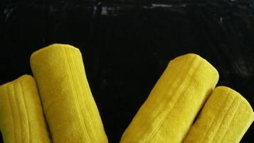 A bed with white linens and two gray pillows. Below the bed, there are two rolled-up yellow towels on a black surface.