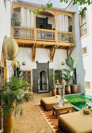A traditional courtyard with a wooden balcony, potted plants, a seating area, and a small pool. - Riad le Jardin Des Sens (Marrakech)