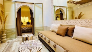 Un interior tradicional marroquí con un sofá, un pouf estampado y un espejo decorativo.