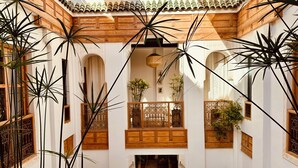 Un patio con balcón de madera, arcos y macetas con plantas.