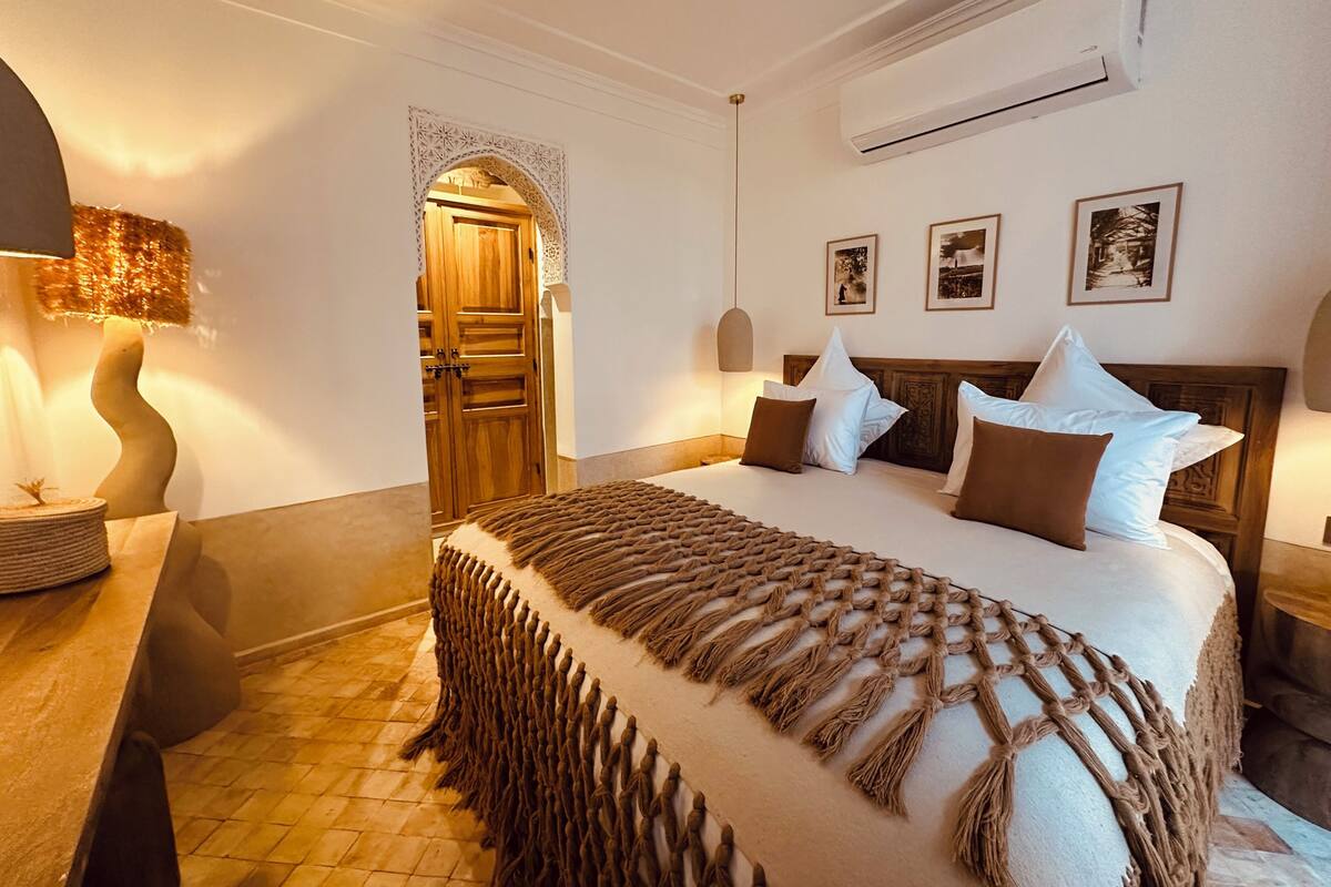 A hotel room with a large bed, a wooden door, a wall-mounted air conditioner, and framed pictures.