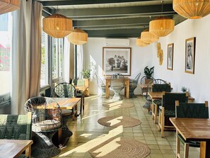 Un interior de restaurante con mobiliario de mimbre, mesas de madera, lámparas colgantes de mimbre y un suelo de baldosas.