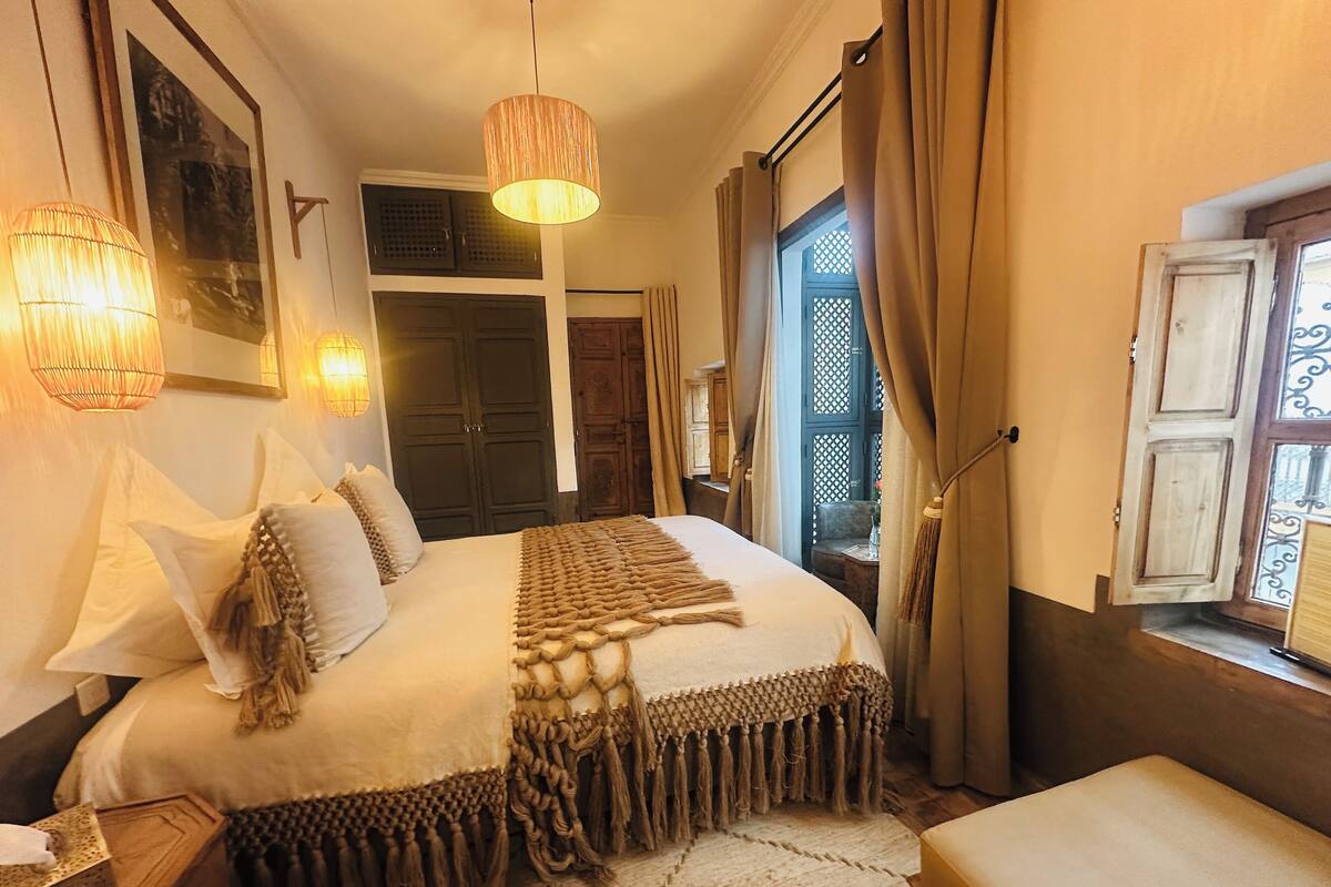 A neatly arranged bedroom with a bed, bedside tables, a hanging lamp, and a window with curtains.