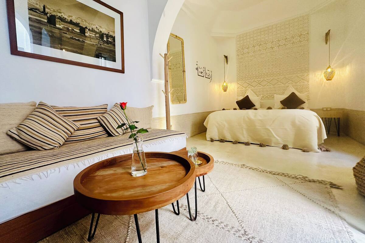 A bedroom with a bed, a sofa, a coffee table, and a wall-mounted mirror.