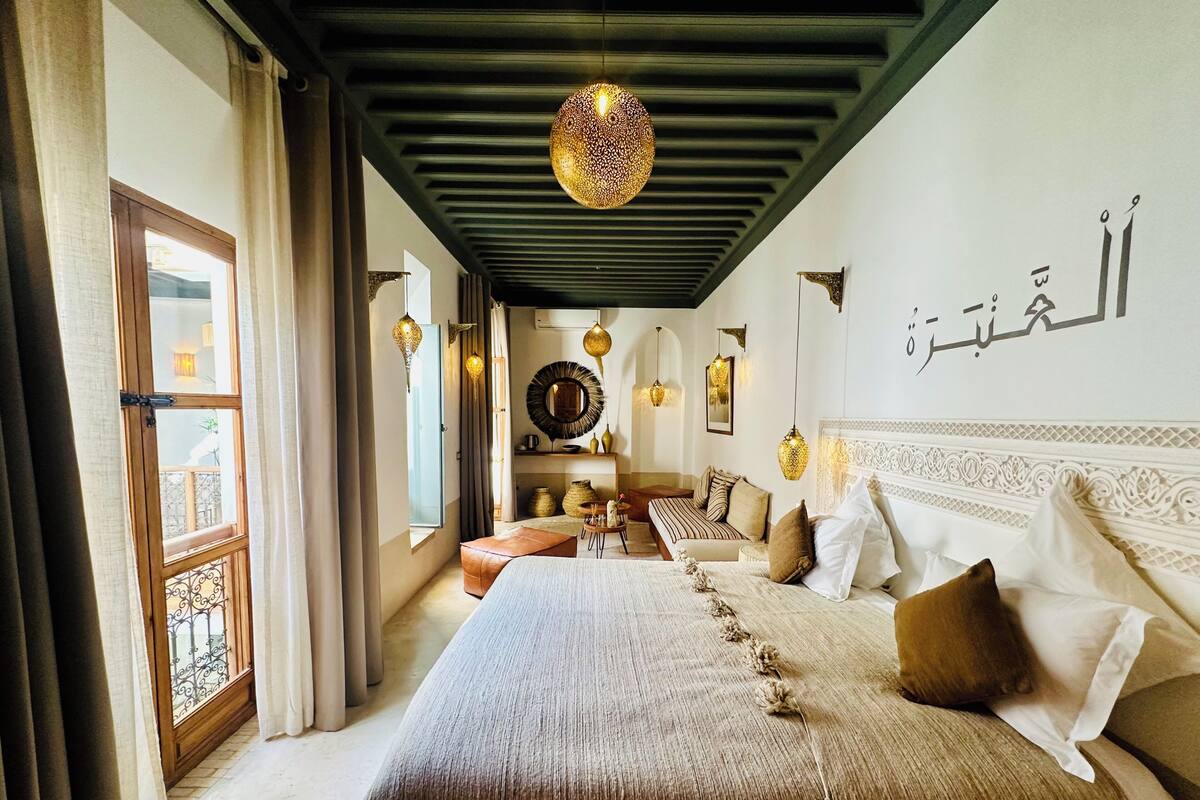 A hotel room with a large bed, a sitting area, and a view through a window.