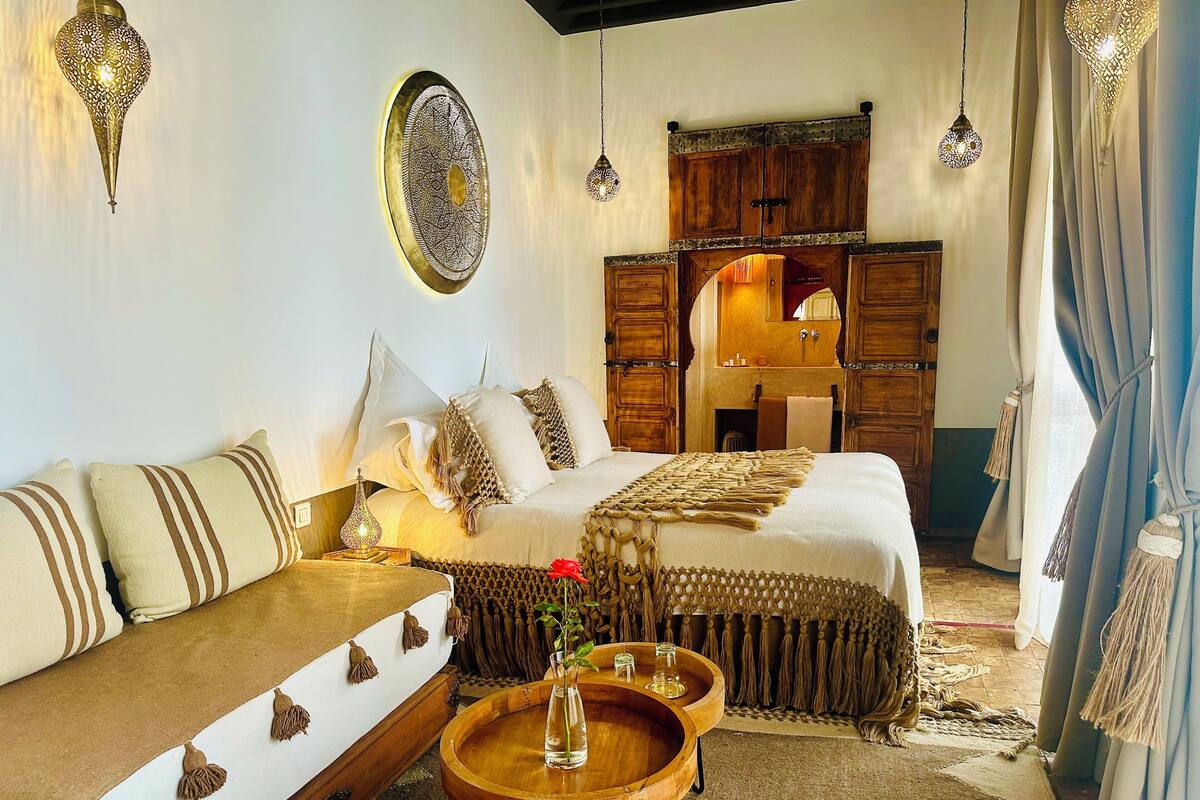A room with a bed, a sofa, a small table with a vase, and a hanging light fixture.