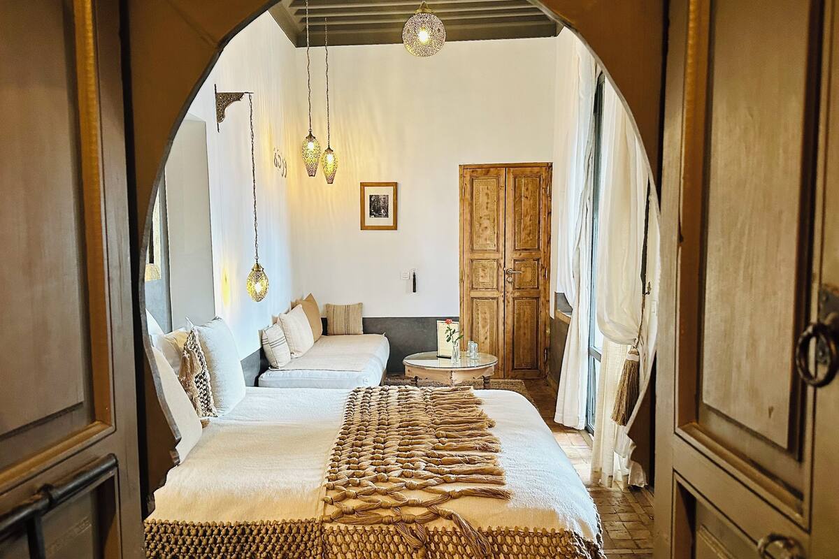 A bedroom with a large bed, a small round table, and a wooden wardrobe.