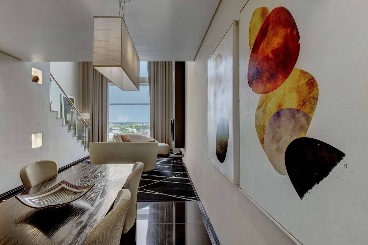A modern hotel lobby with a dining area, a staircase, and large abstract wall art.