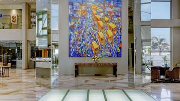 A spacious lobby with a large abstract painting, a marble floor, and a reception desk with chairs.