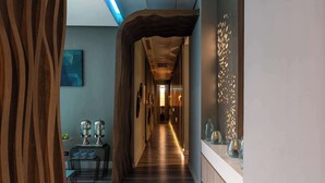 Un pasillo con suelo de madera, un comedor con mesa y sillas, y una pared decorativa con jarrones de vidrio.