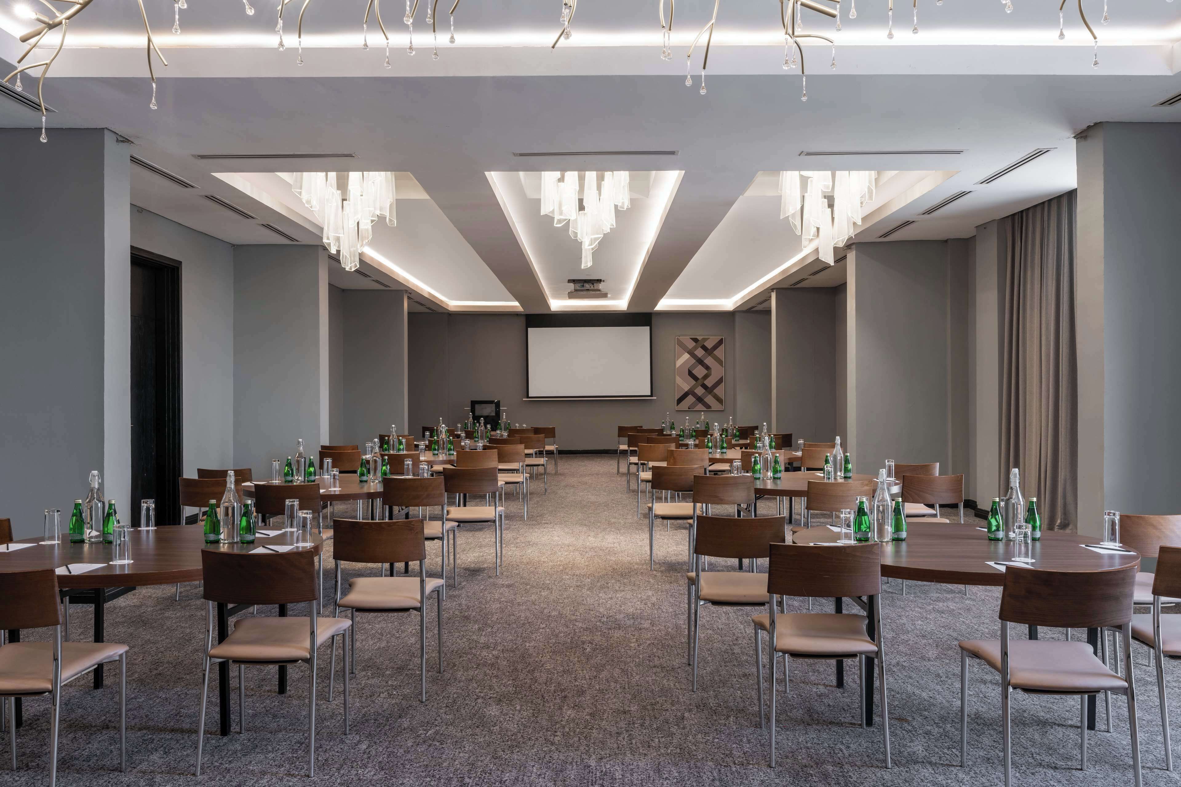 A conference room with multiple tables, chairs, and a projector screen.