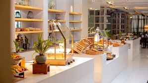 Un café moderno con un diseño limpio y minimalista, que presenta estantes de madera, diversos productos alimenticios y plantas decorativas.
