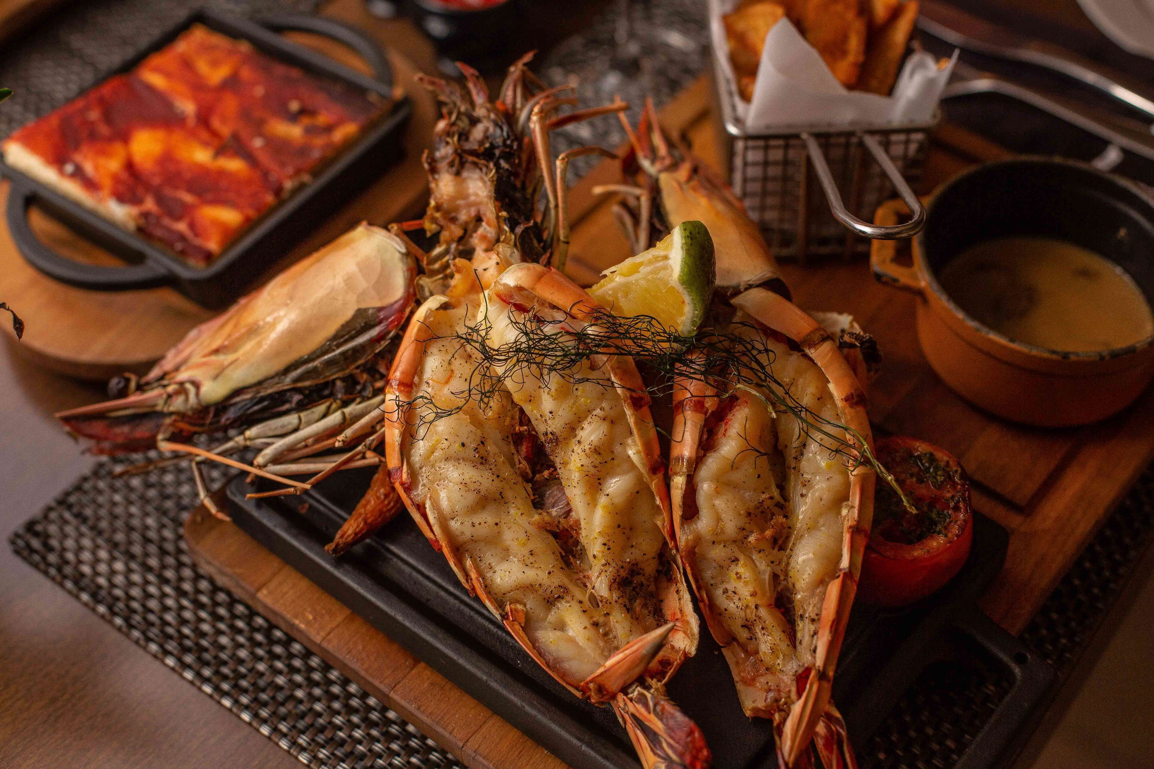 A seafood platter with grilled shrimp, a baked potato, and a small bowl of sauce.