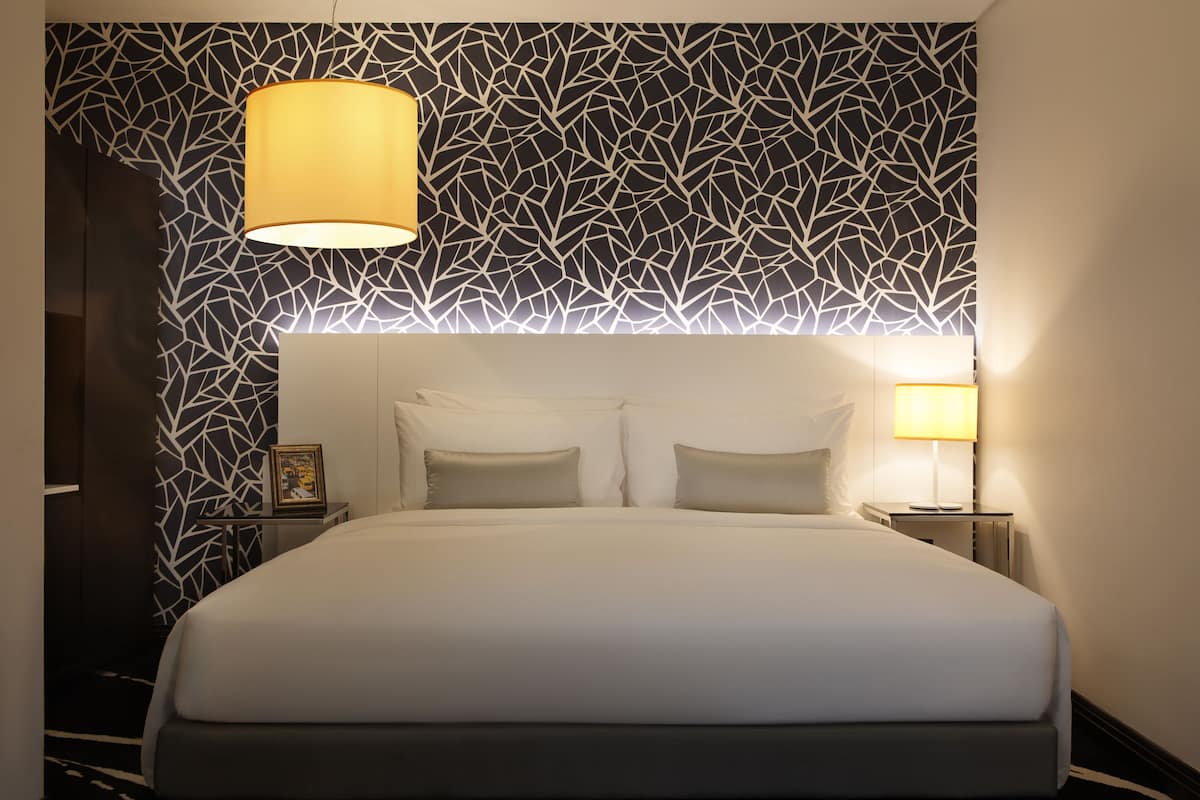 A neatly made bed with a headboard, a bedside table with a lamp, and a wall with a geometric pattern.