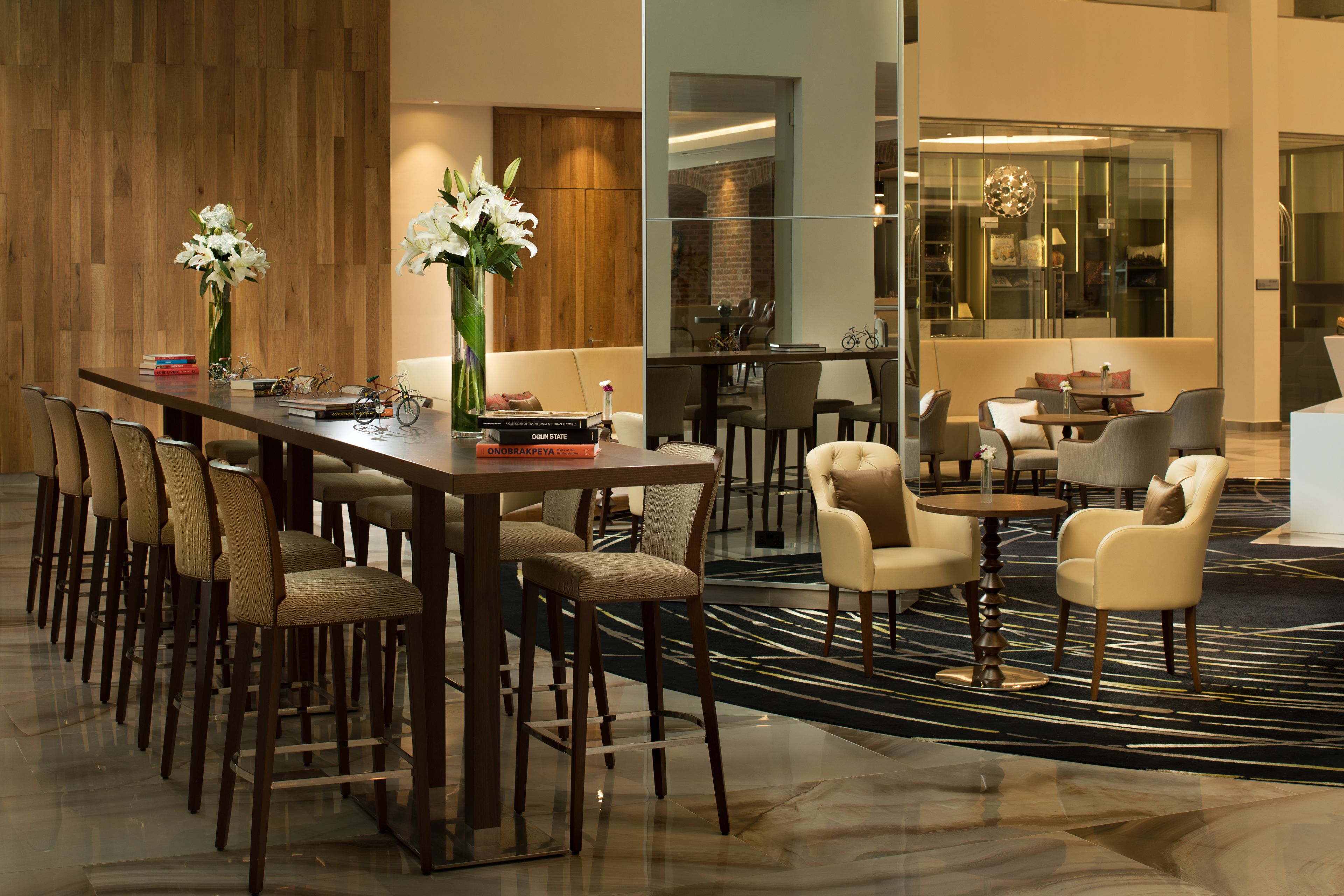 A modern hotel lobby with a long reception desk, multiple seating areas, and a large window offering a view of the interior.