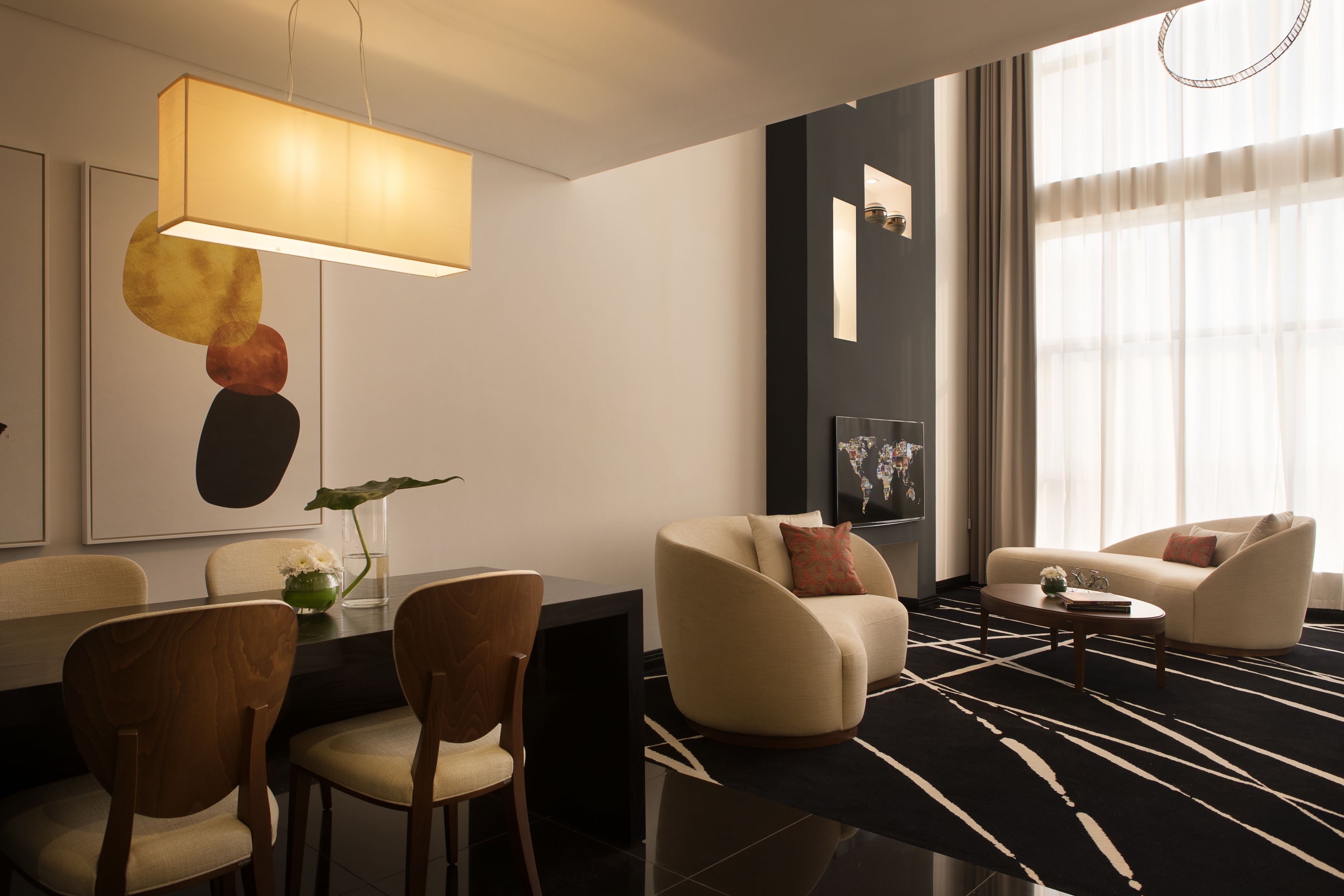 A modern hotel room with a dining area, two sofas, a coffee table, and a large window with curtains.