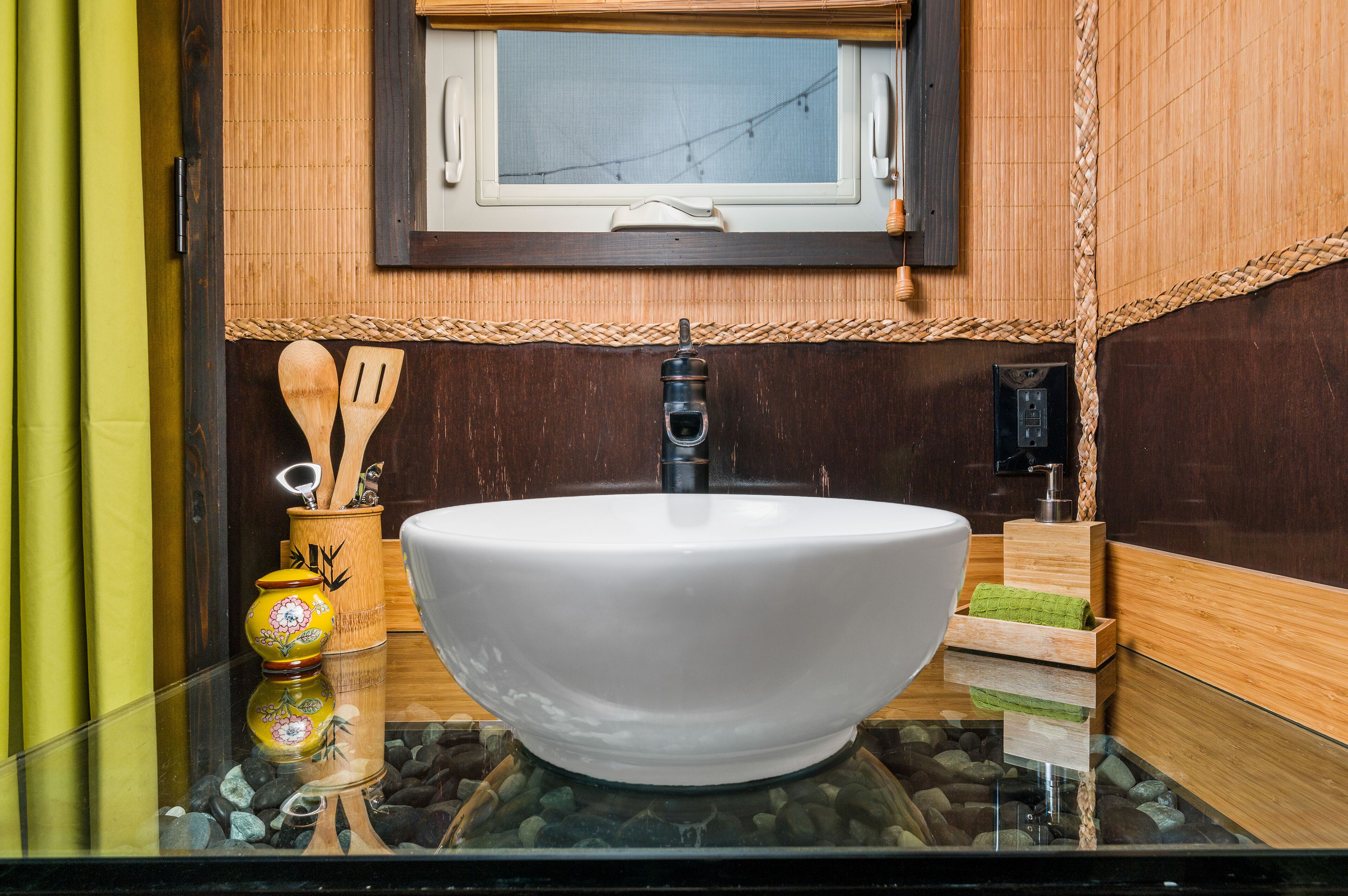 A bathroom with a large white sink, wooden wall decor, and a window above the mirror.