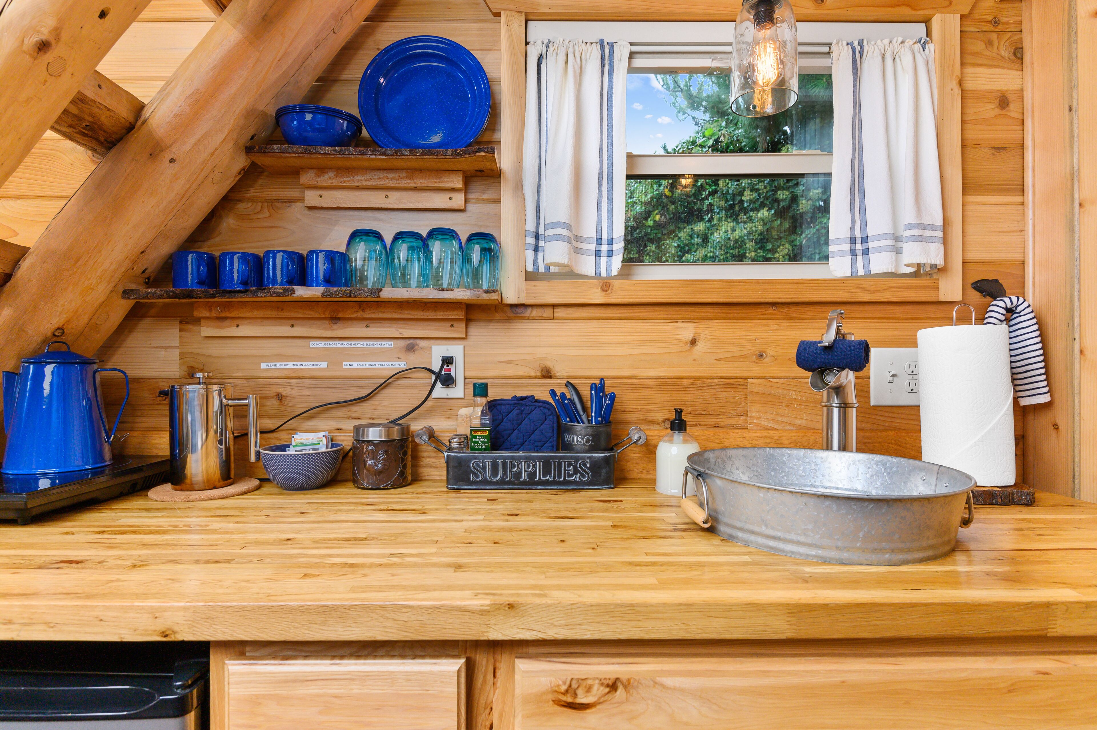 Cocina de cabaña de madera con un lavamanos de metal, vajilla azul y un letrero que dice 'SUPPLIES'.