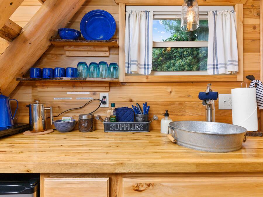 Cocina de cabaña de madera con un lavamanos de metal, vajilla azul y un letrero que dice 'SUPPLIES'.
