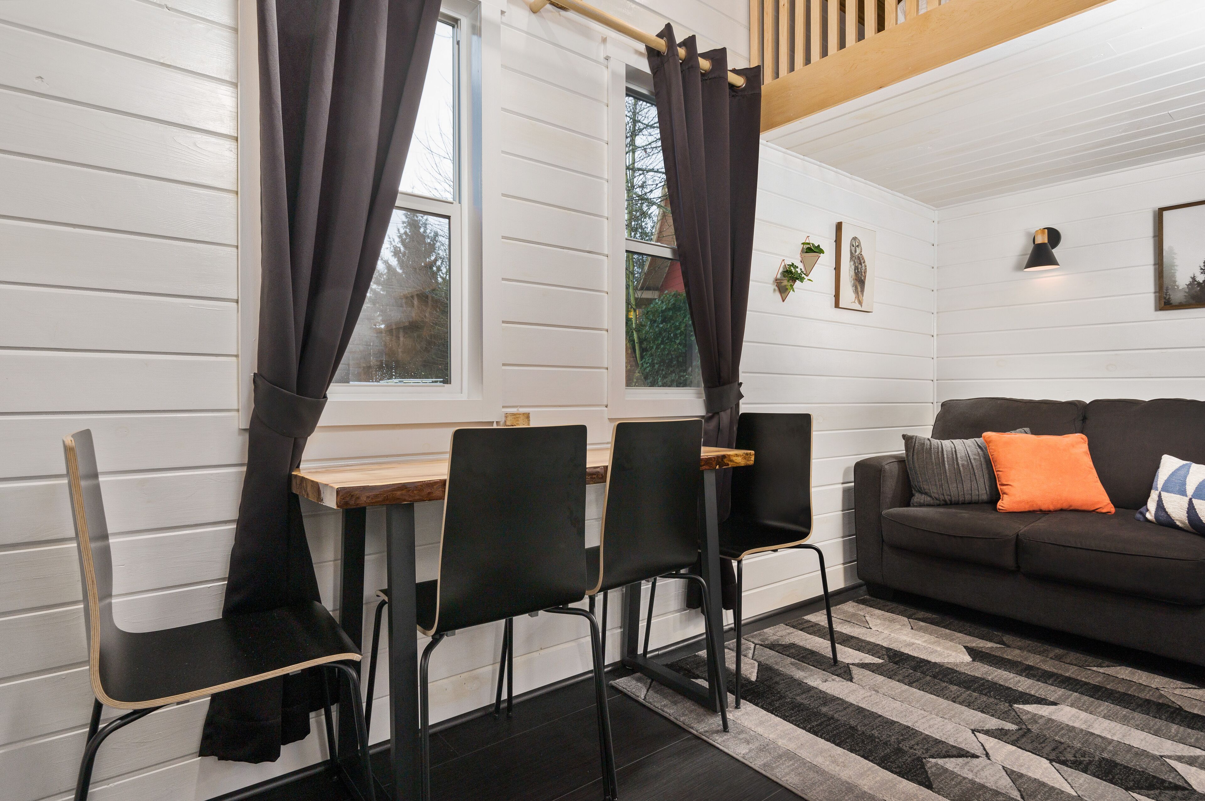 Ein gemütliches Zimmer mit Esstisch, Stühlen, einer Couch und einem Fenster mit Vorhängen.