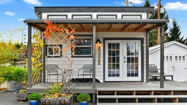 A small, single-story building with a covered porch, a dining area with chairs, and a small garden with potted plants. - Tiny Digs - Hotel of Tiny Houses (Portland)