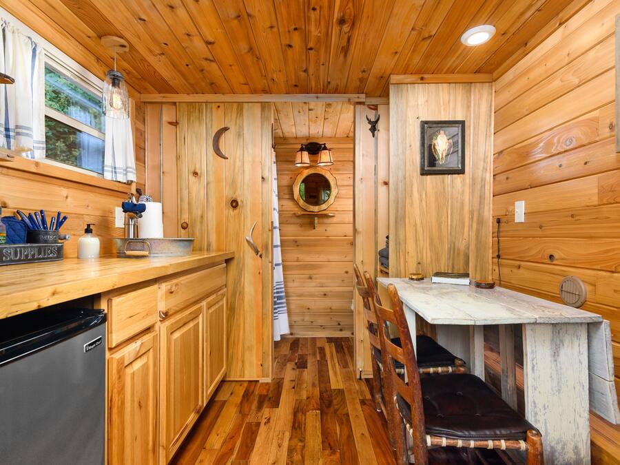 A wooden cabin interior with a kitchen area, wooden walls, and a dining table.