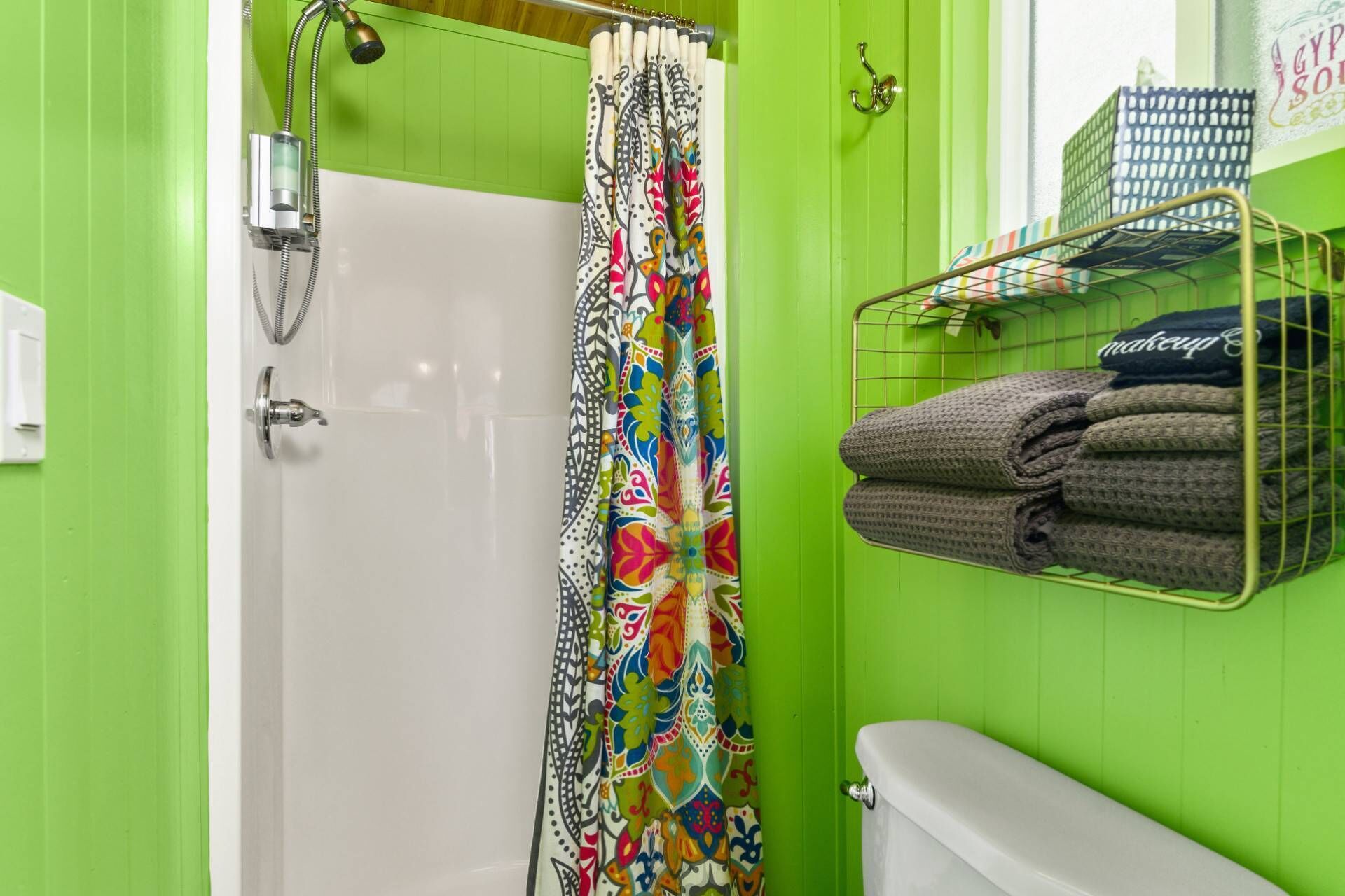 A bathroom with a shower, toilet, and a towel rack with folded towels.