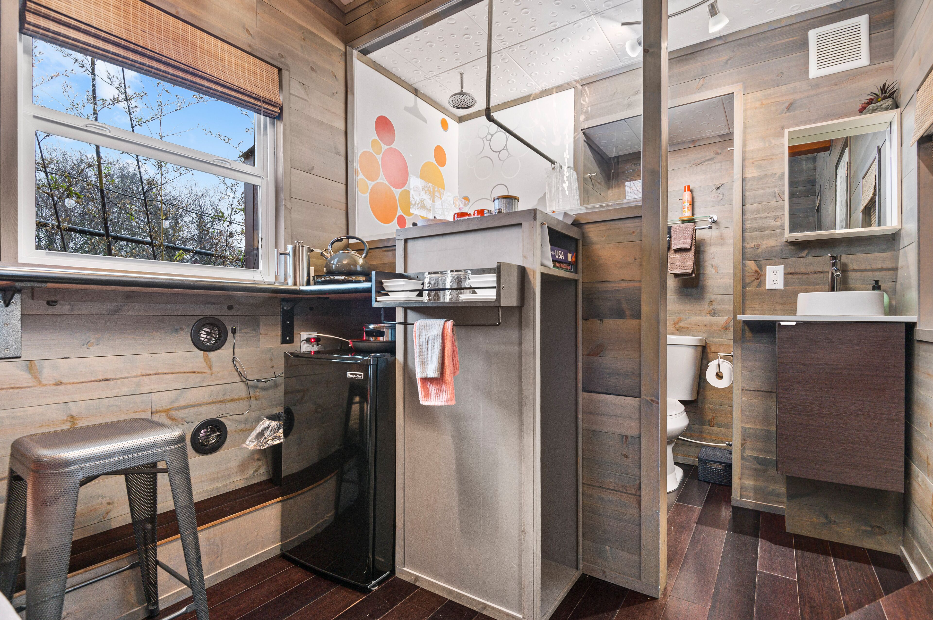 A compact kitchen with a refrigerator, a sink, and a window overlooking trees.