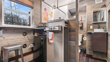 A compact kitchen with a refrigerator, a sink, and a window overlooking trees.
