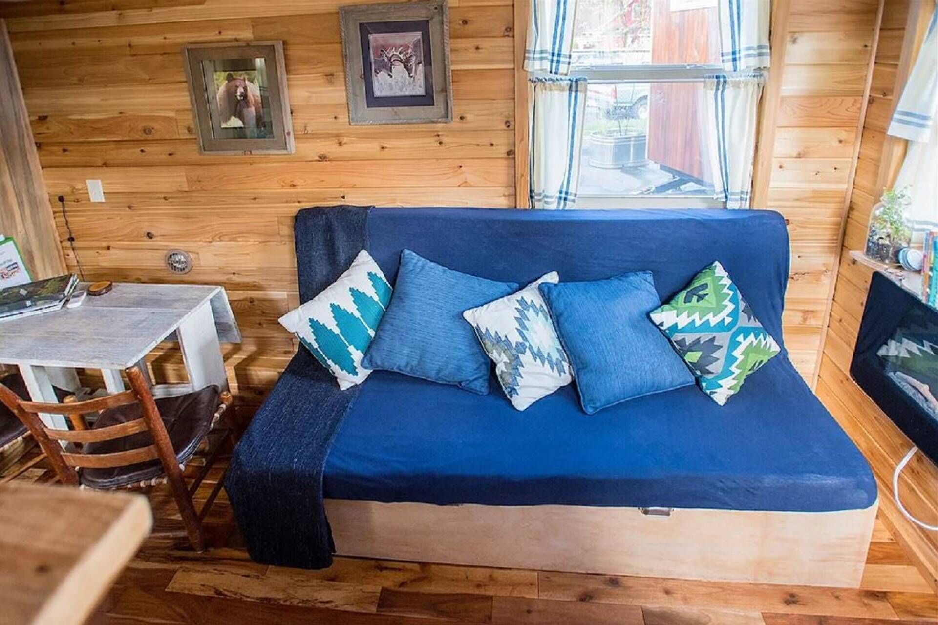 Een gezellig cabin interieur met een blauwe bank, houten wanden, een kleine tafel en lijstjes met foto's aan de wand.