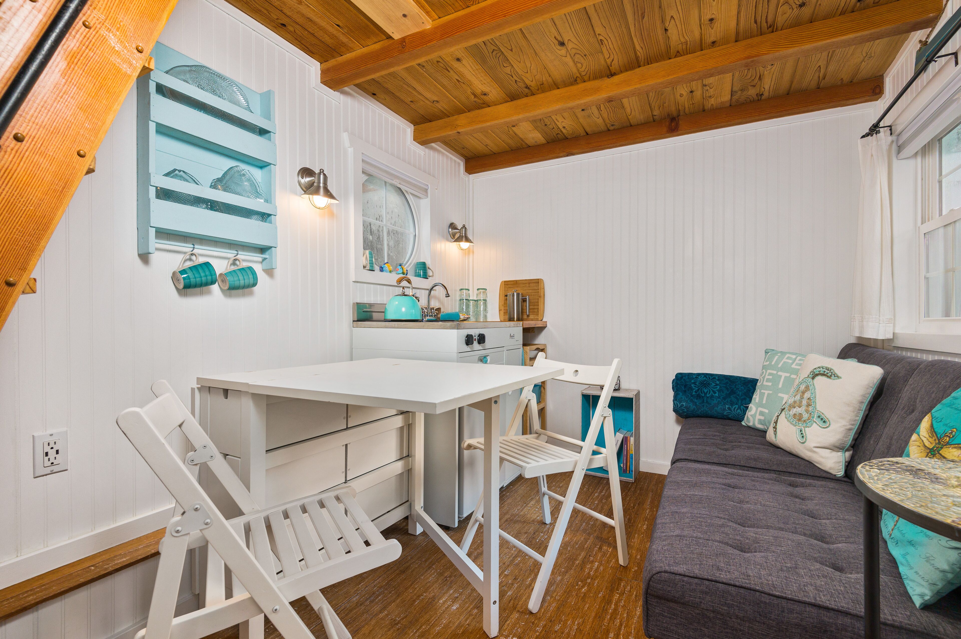 A cozy kitchen with white cabinetry, a wooden ceiling, and a dining area with white chairs.