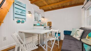A cozy kitchen with white cabinetry, a wooden ceiling, and a dining area with white chairs.