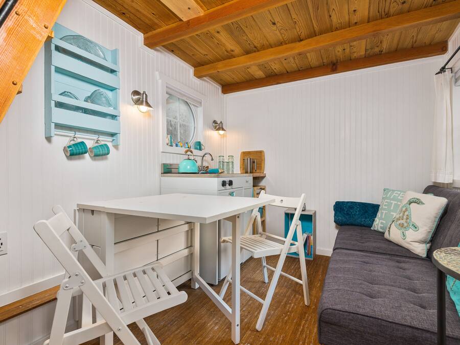 Une cuisine chaleureuse avec des meubles blancs, un plafond en bois et un coin repas doté de chaises blanches.