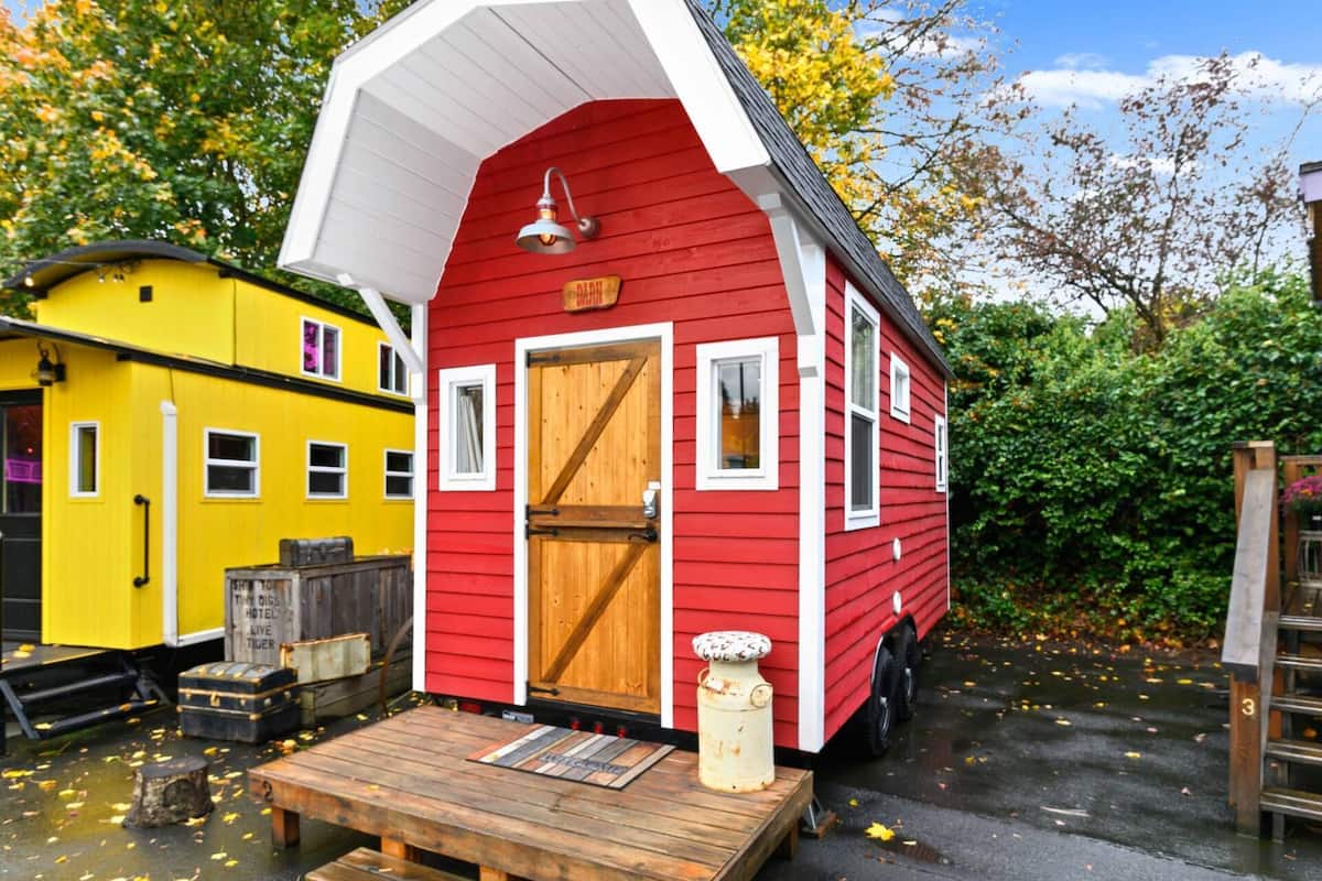 A red mobile home with a white roof, a wooden door, and a small porch with a bench.