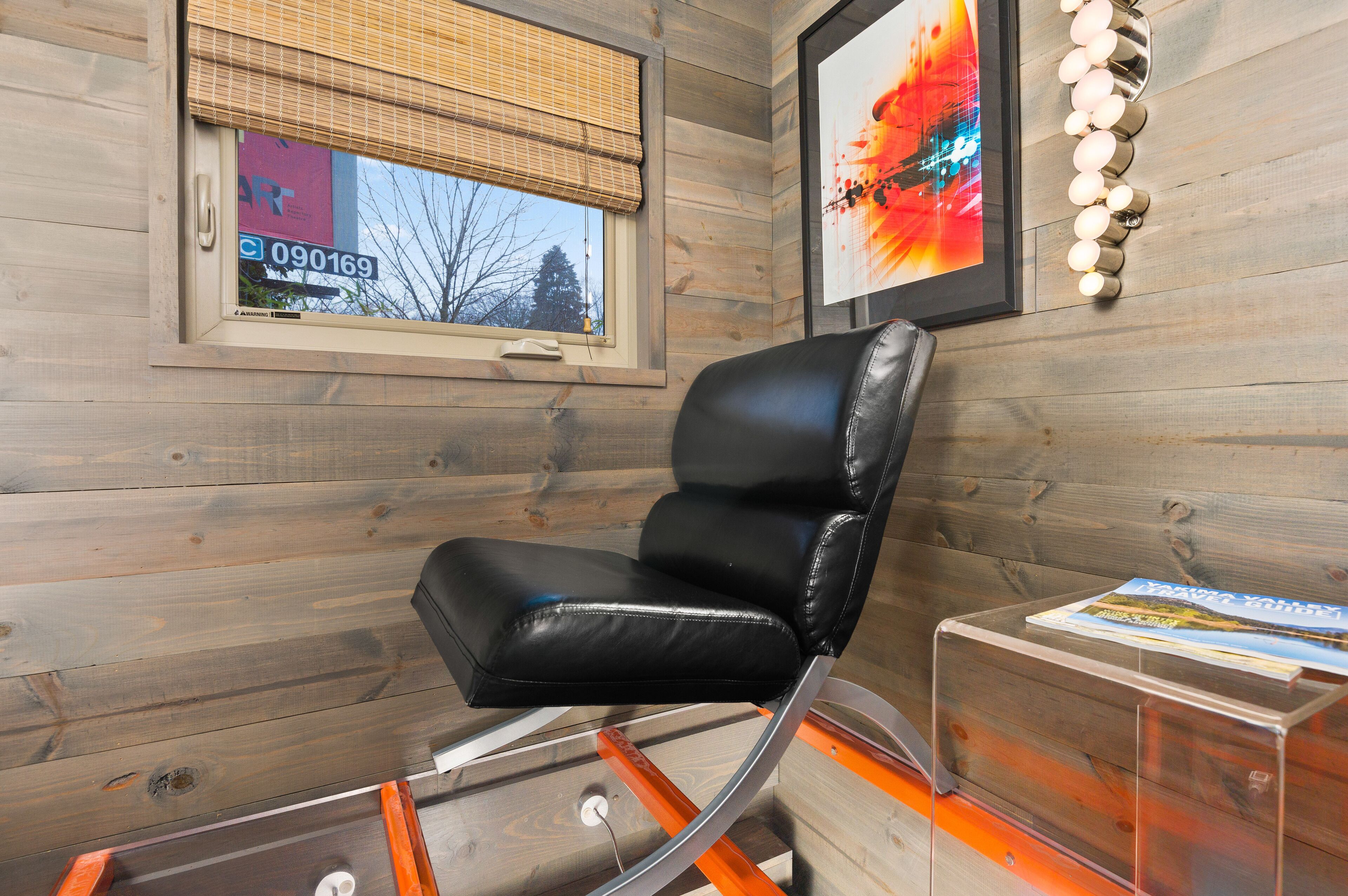 A modern room with a black leather chair, a clear glass table, and a framed abstract painting on the wall.