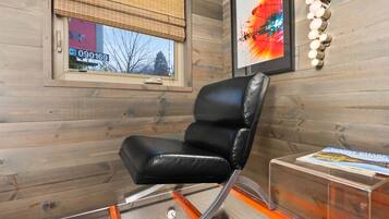 A modern room with a black leather chair, a clear glass table, and a framed abstract painting on the wall.