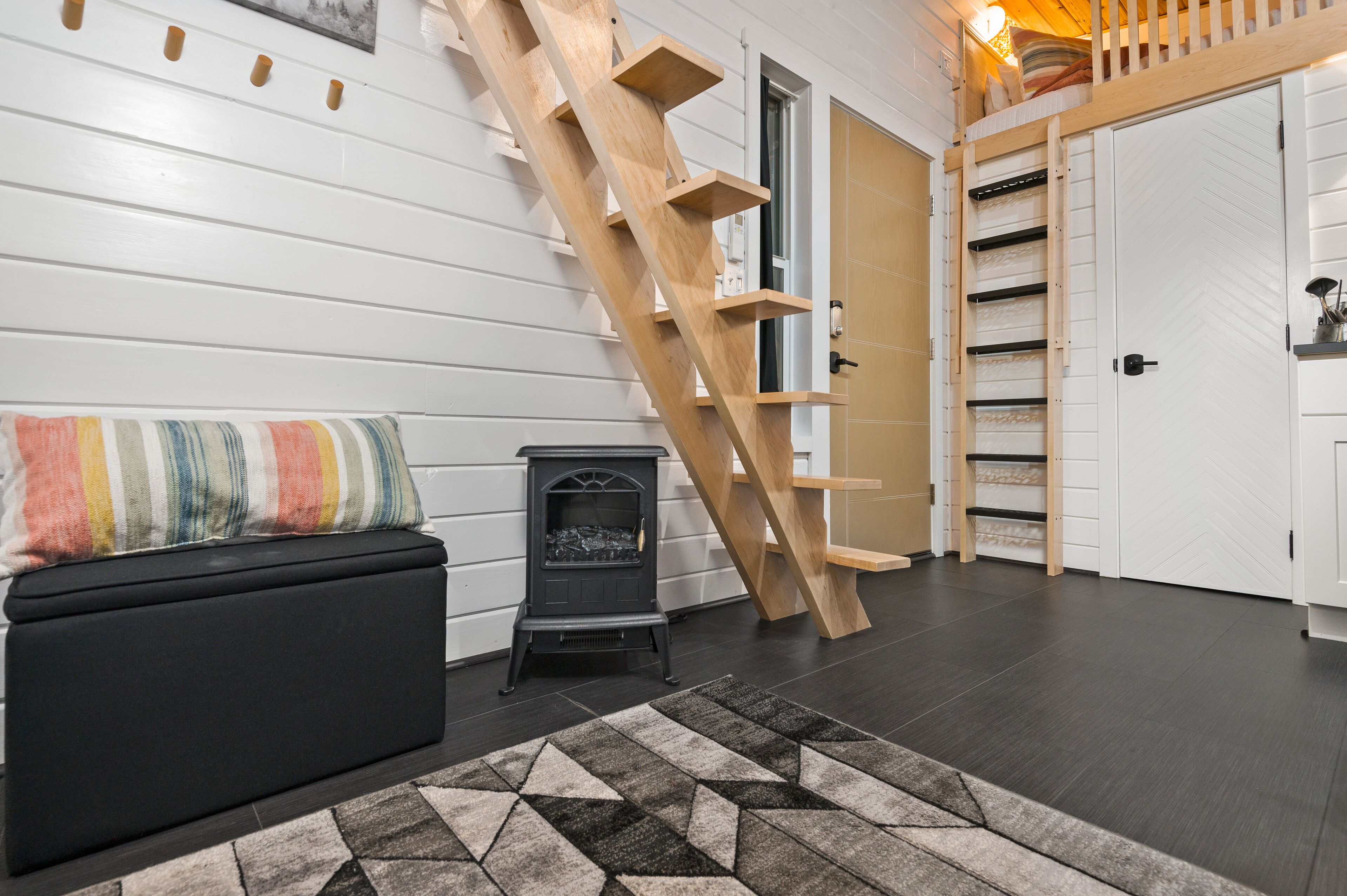 A cozy room with a wooden staircase, a black sofa with a striped cushion, and a fireplace.