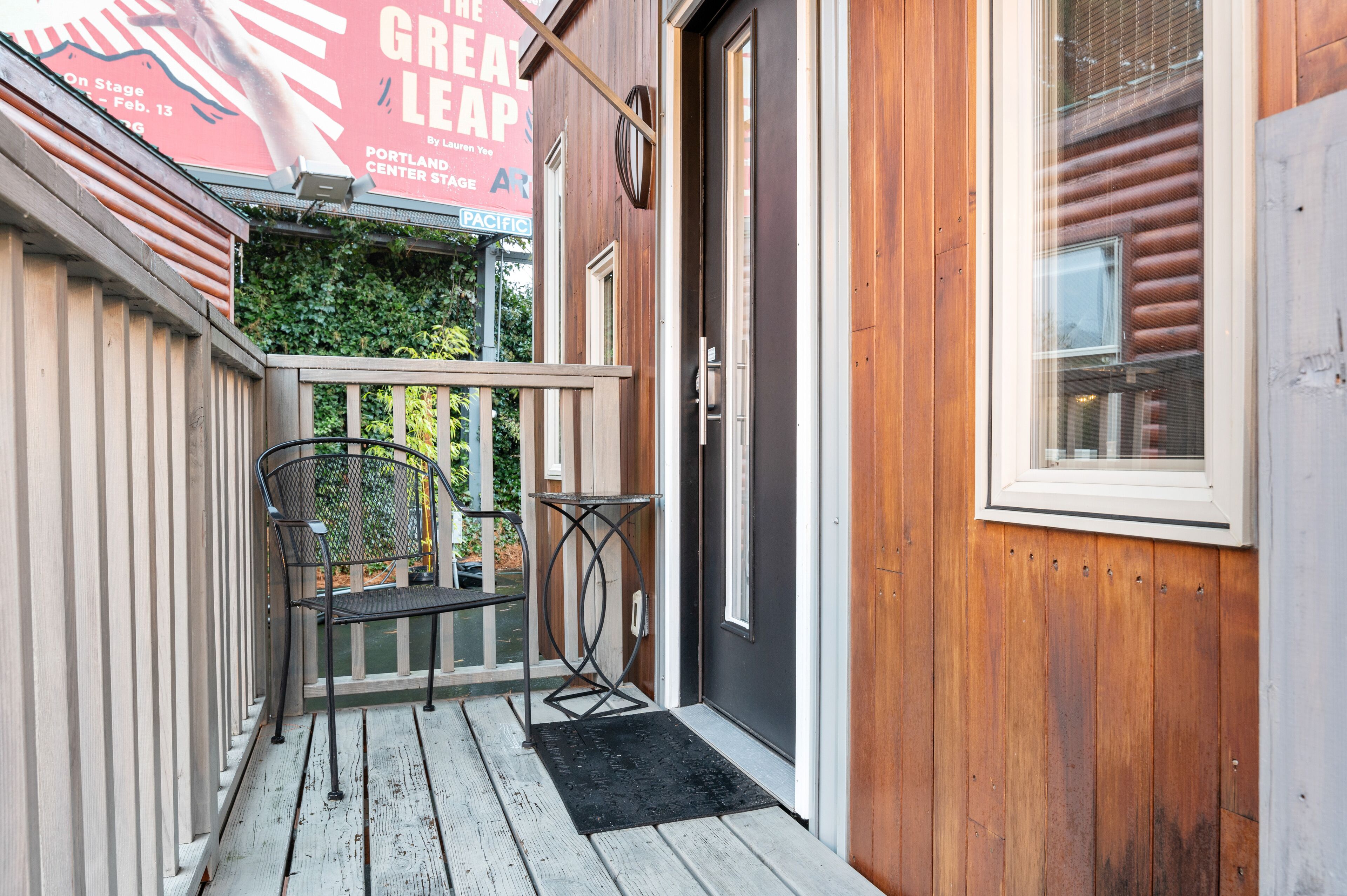 A wooden exterior with a black door and a small porch area with a chair and table.