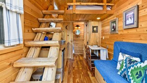 A wooden cabin interior with a loft bed, a sofa, and a dining area. - Tiny Digs - Hotel of Tiny Houses (Portland)