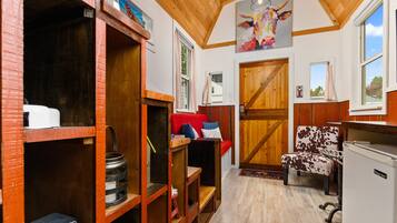 A rustic interior with wooden shelves, a red sofa, a cow-themed chair, and a wooden door.