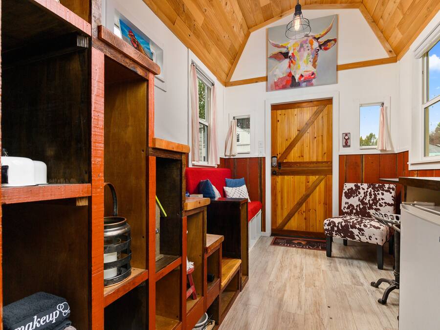 A rustic interior with wooden shelves, a red sofa, a cow-themed chair, and a wooden door.