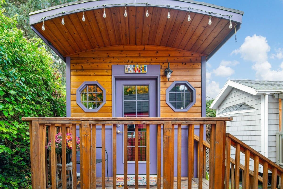 A wooden cabin with a purple door, two octagonal windows, and a wooden deck.