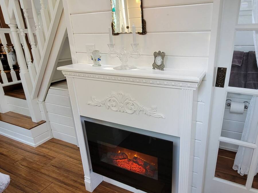 Una chimenea blanca con puerta de vidrio, un rodapié con adornos y una escalera con barandillas blancas.