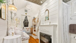 A room with a fireplace, wooden flooring, a bed with floral bedding, a small table, and a chandelier. - Tiny Digs - Hotel of Tiny Houses (Portland)