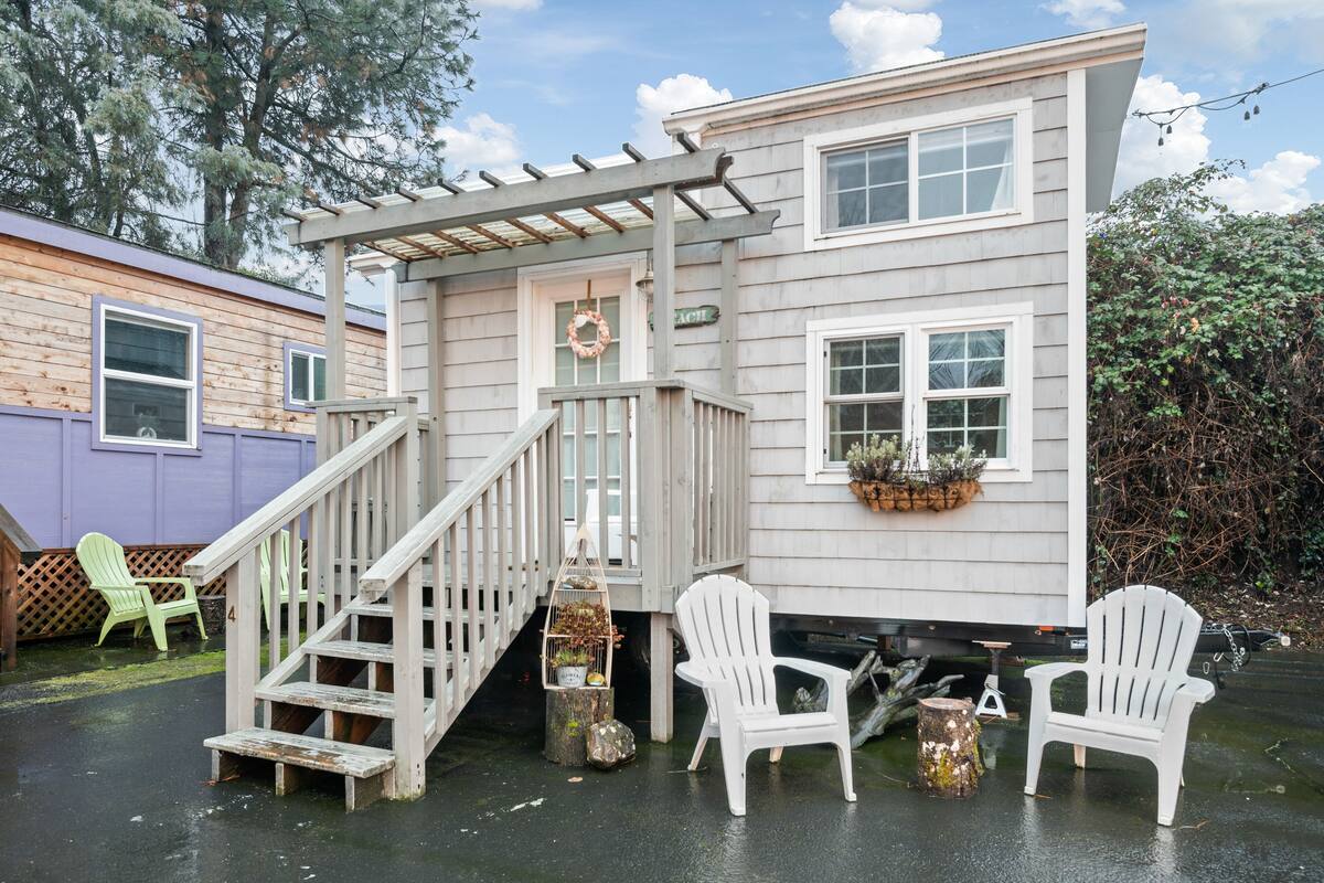 A two-story house with a porch, a wooden staircase, and two white Adirondack chairs.
