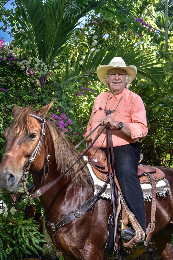 Una persona montando a caballo en un entorno exuberante, verde, con follaje denso y plantas con flores.