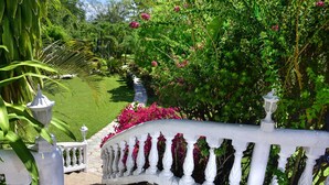Una balaustrada blanca de diseño curvo que conduce a un exuberante jardín con césped verde y flores rosas.