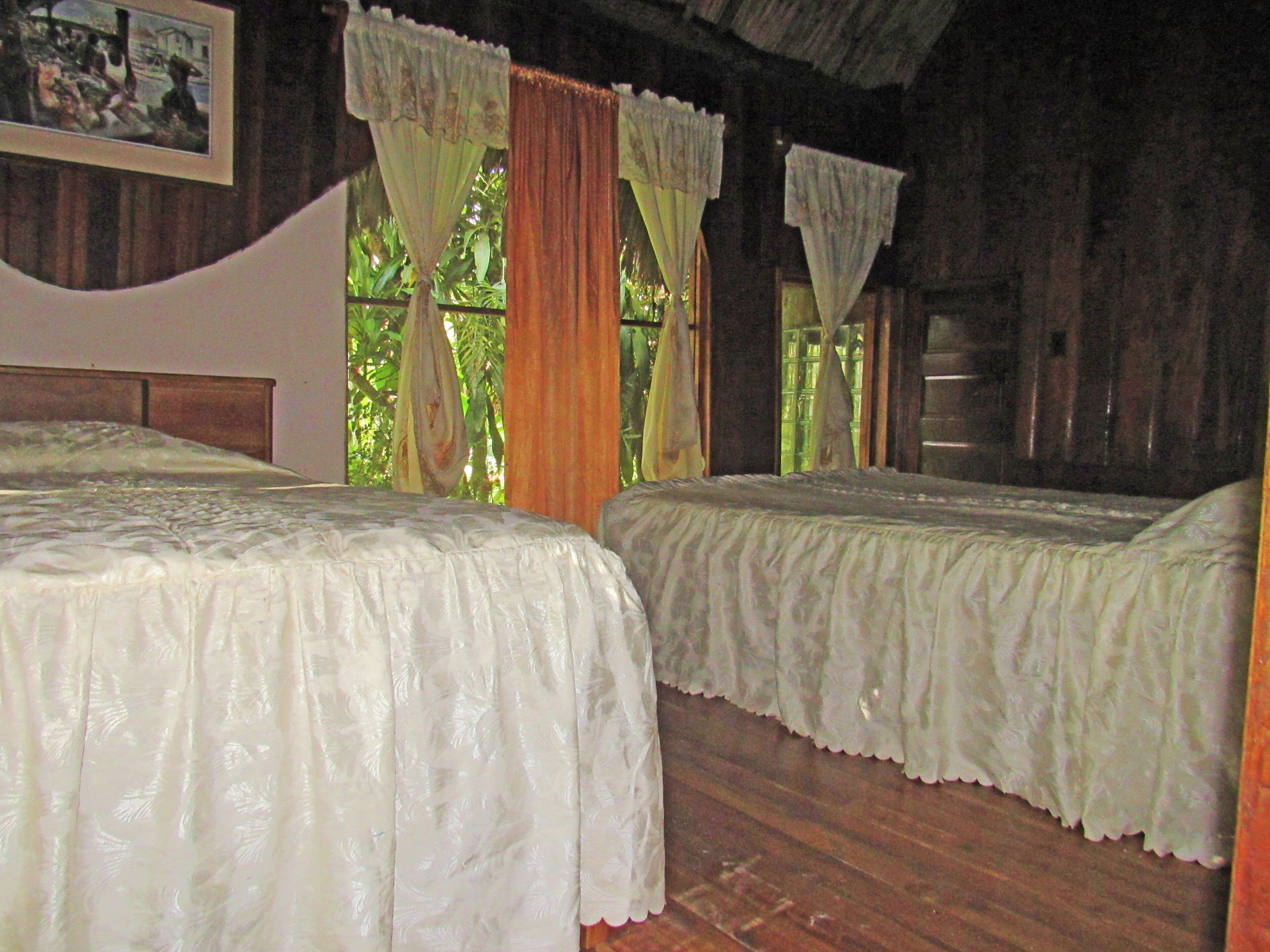 A room with two beds, wooden walls, and a window with curtains.
