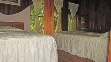 A room with two beds, wooden walls, and a window with curtains.